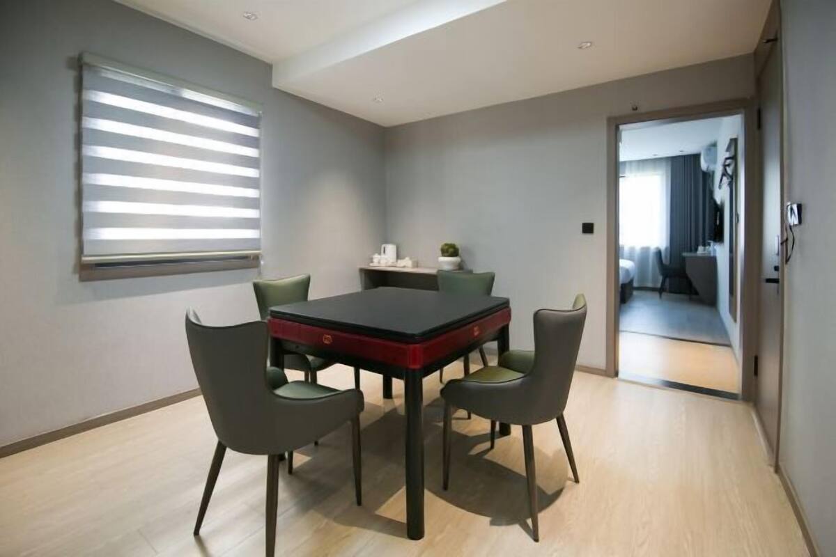 A modern dining area with a rectangular table and six chairs, a window with blinds, and a view into another room.