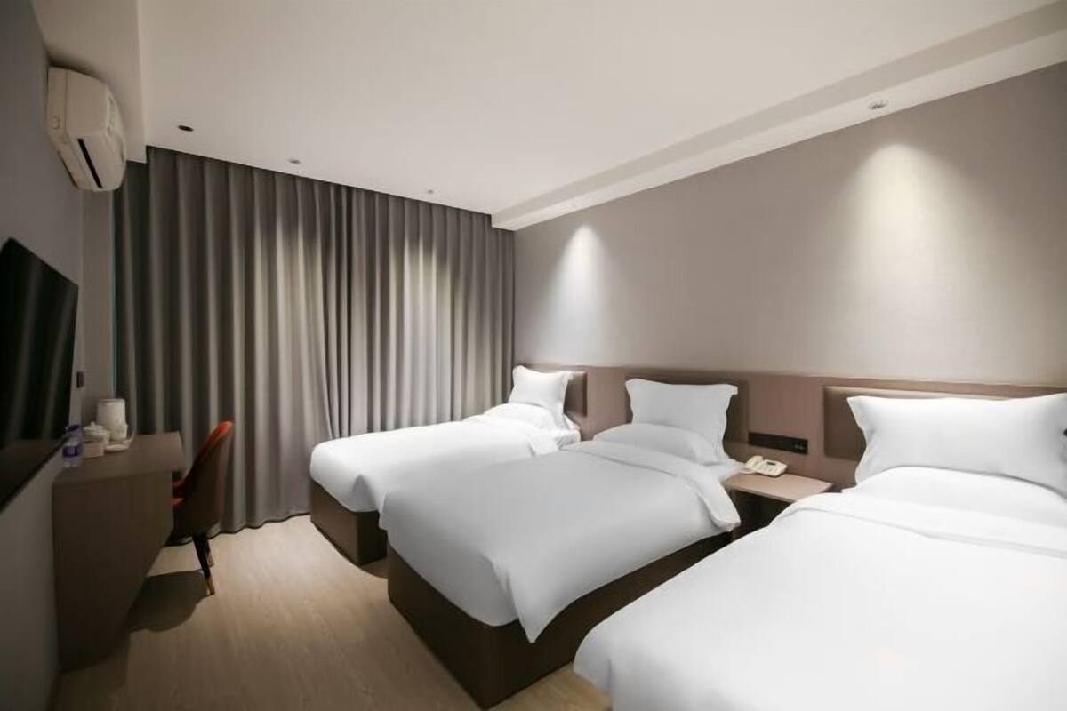 A hotel room with two beds, a desk, a chair, and a TV.