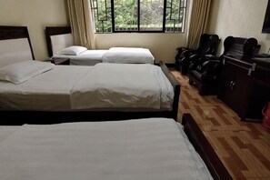 Habitació d'hotel amb tres llits, un sòl de fusta, una finestra amb cortines i un escriptori amb una cadira.