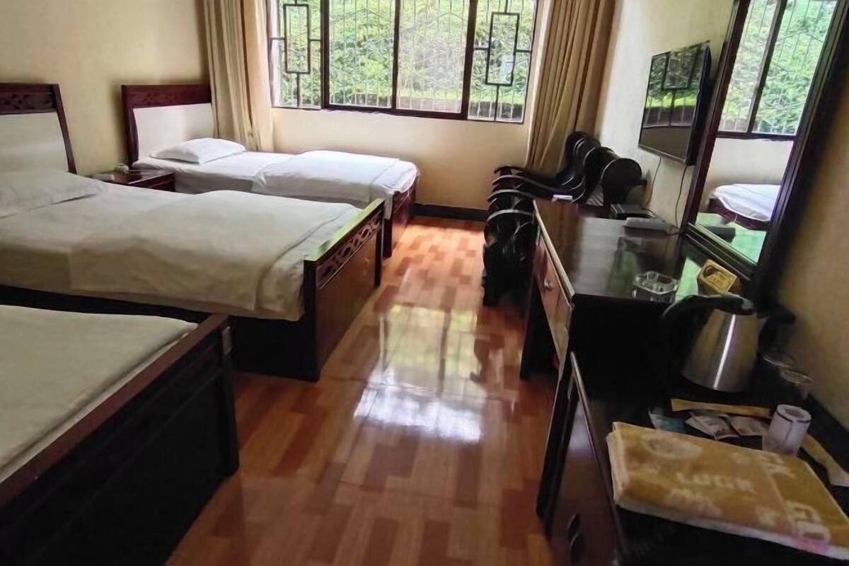 Una habitación de hotel con dos camas, un escritorio con hervidor, televisión y ventana con cortinas.
