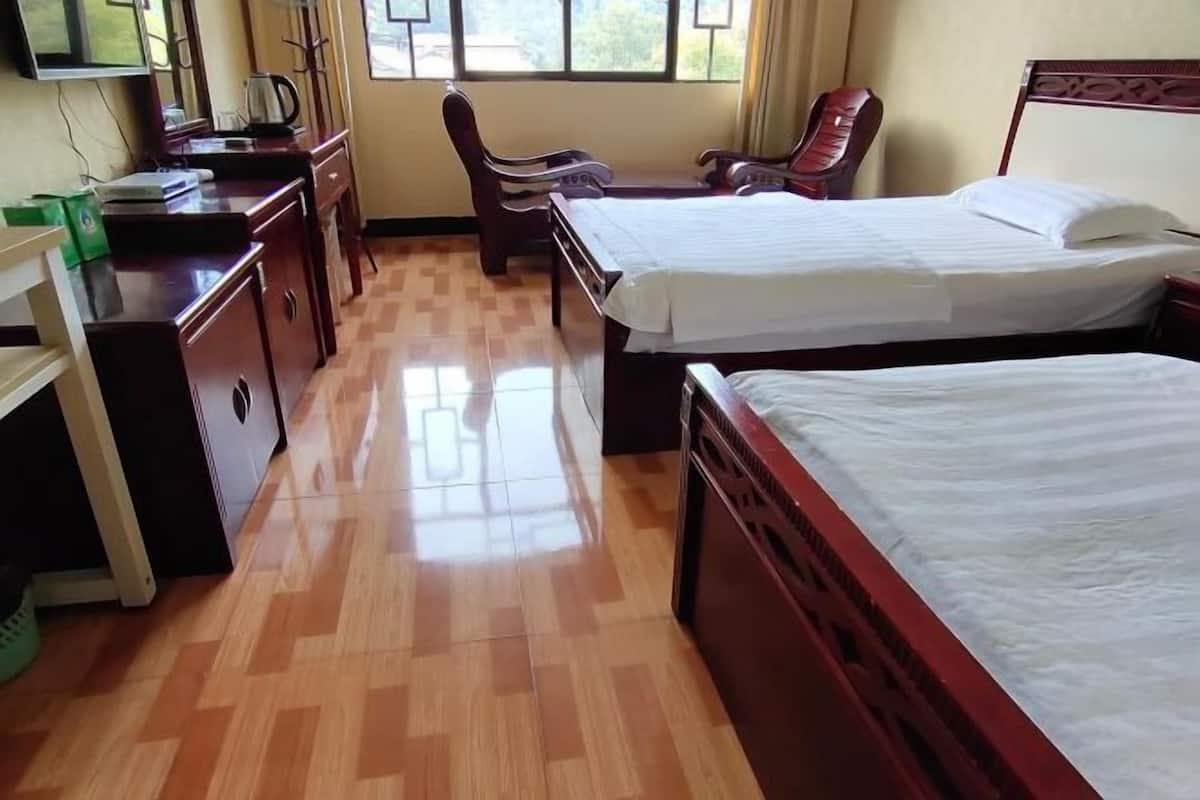 Una habitación de hotel con dos camas, un escritorio con silla, televisión y ventana con cortinas.