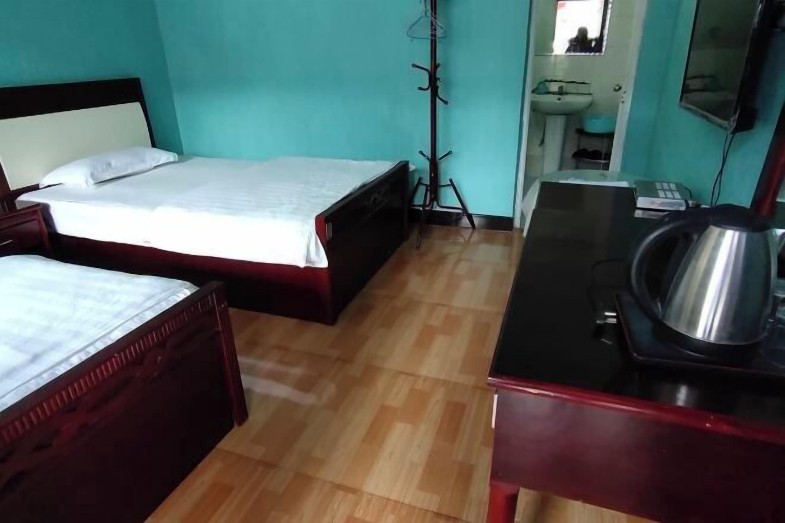 A room with two beds, a desk with a kettle, a sink, and a mirror.