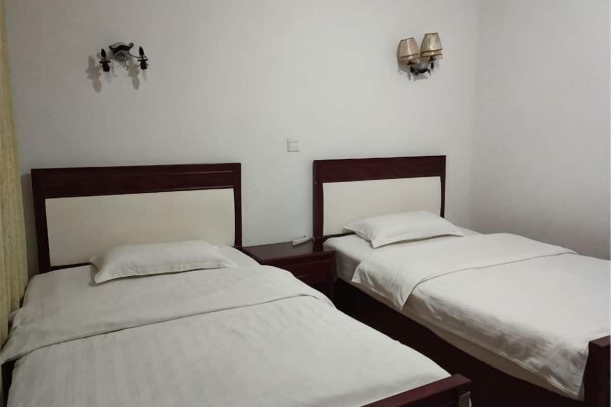 Dos camas individuales con cabeceros de madera, ropa de cama blanca y lámparas de noche sobre una pared blanca.