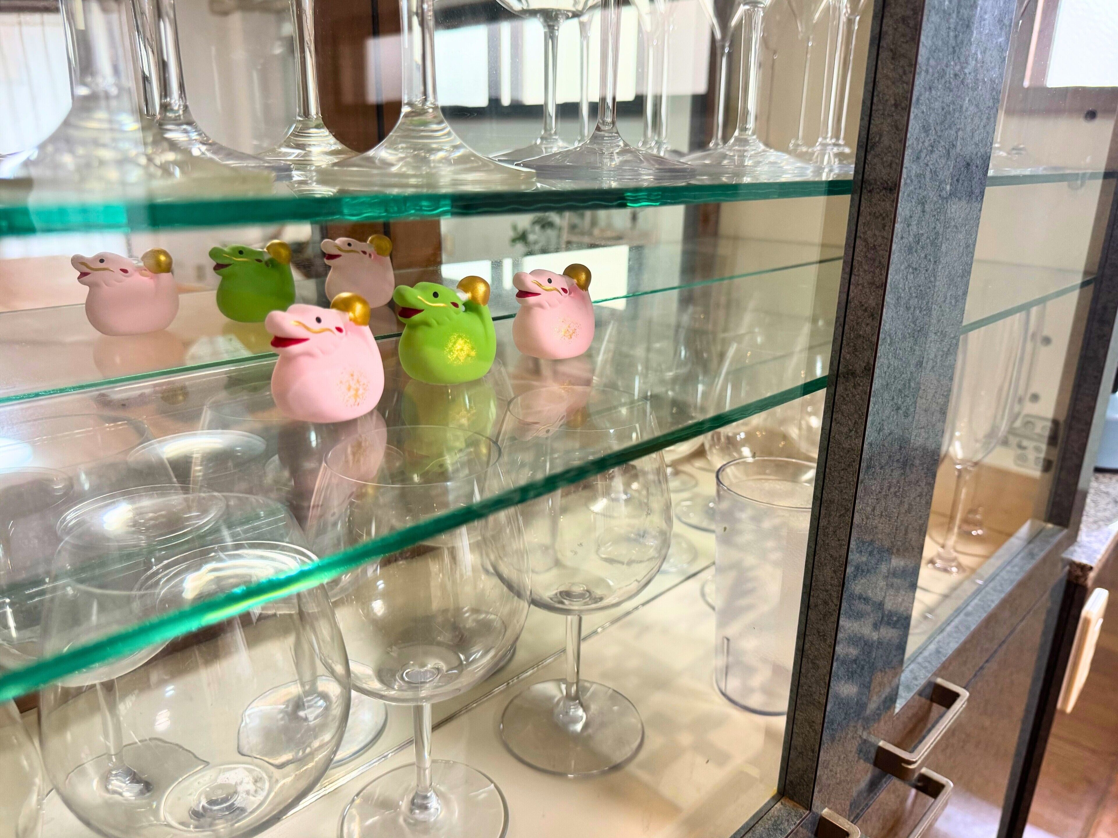 Vitrina de vidrio con copas de vino y figuritas decorativas de cerdos.