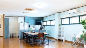 A spacious living area with a wooden floor, a dining table with chairs, a kitchen area with cabinets, and a large window providing natural light.