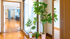 A hallway with wooden flooring, a glass door leading to a room, and potted plants.