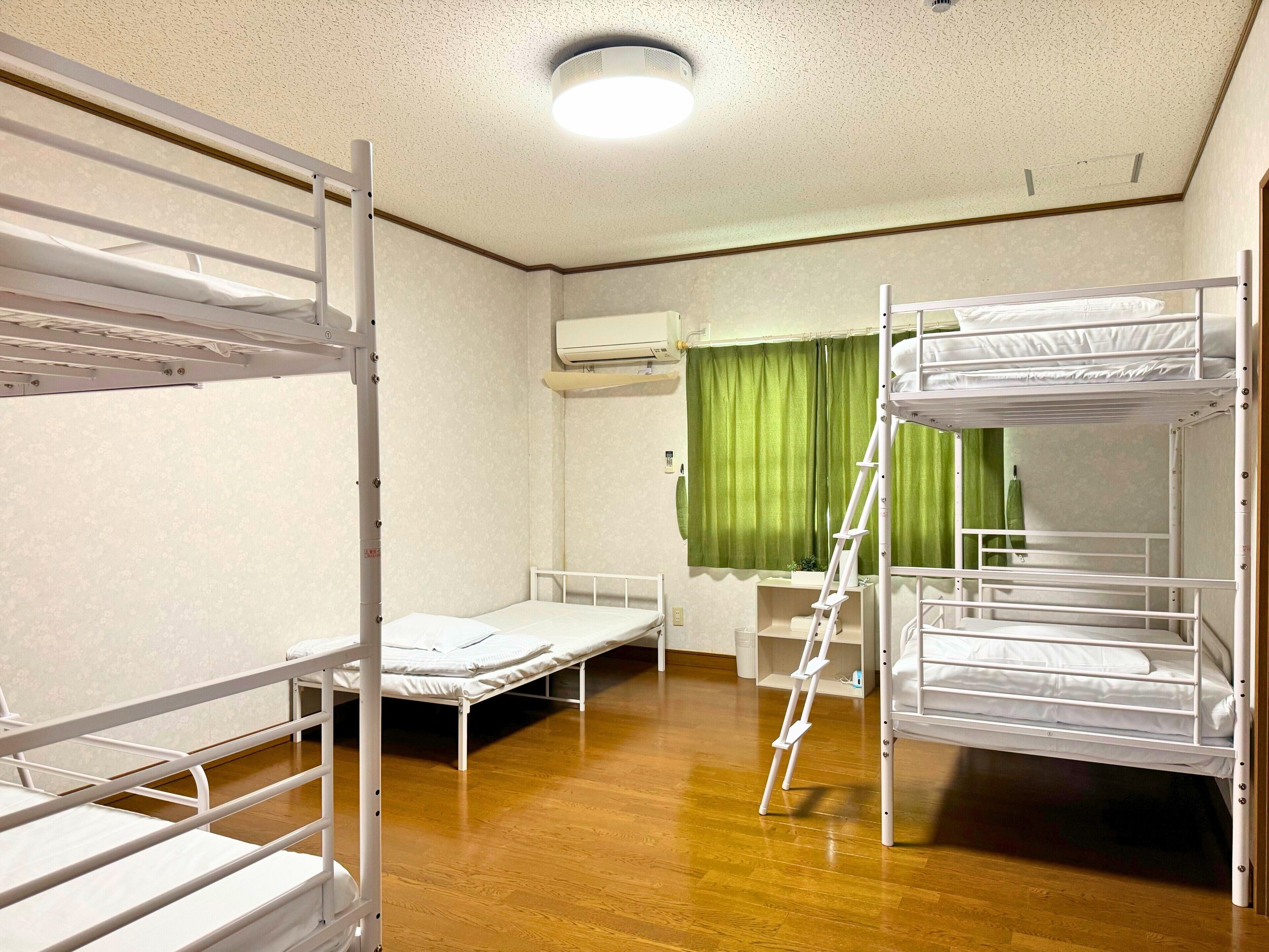 A dormitory room with bunk beds, a ladder, an air conditioning unit, and a green curtain.