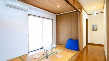 Una habitación japonesa tradicional con suelo de tatami, una puerta corredera, una pequeña mesa con un taburete y un cojín azul.