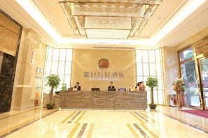 Un hall d’accueil d’hôtel avec un comptoir en marbre, un lustre et un grand logo sur le mur.