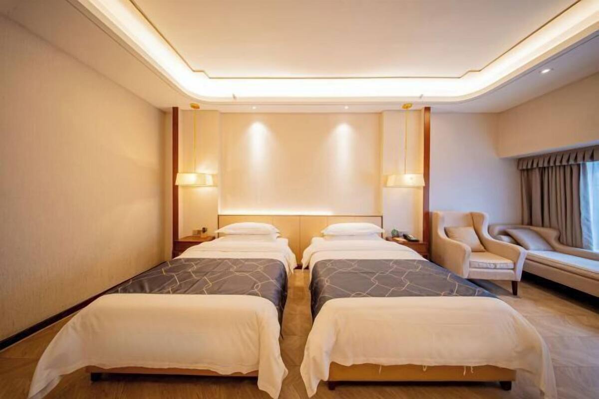 Een hotelkamer met twee bedden, een bank, een stoel en een groot raam.