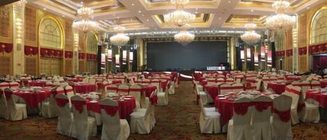 A banquet hall with round tables, white chairs, and red tablecloths.