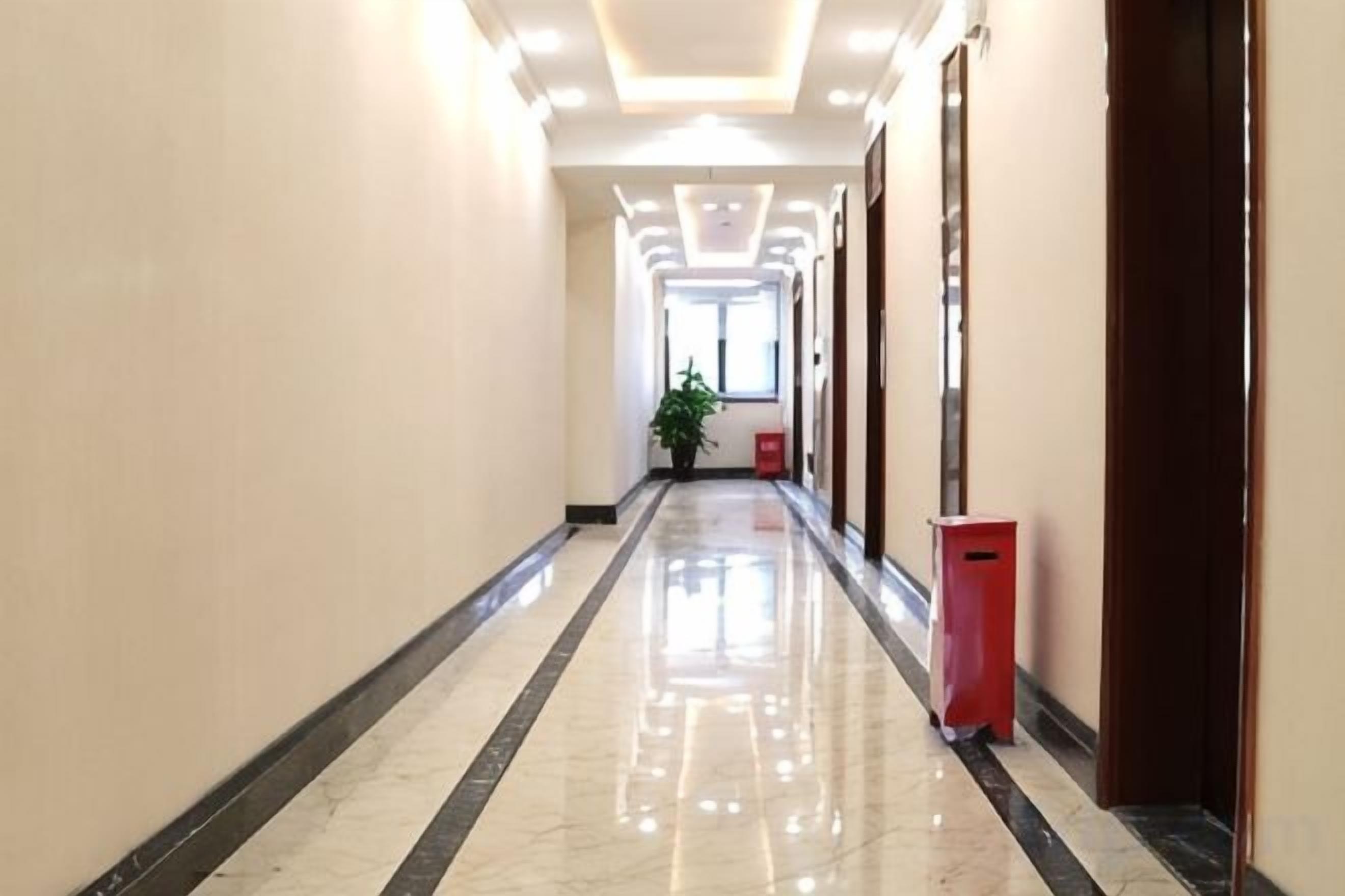 A hallway with a reflective floor, doors on the right, and a trash bin.
