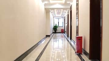 A hallway with a reflective floor, doors on the right, and a trash bin.