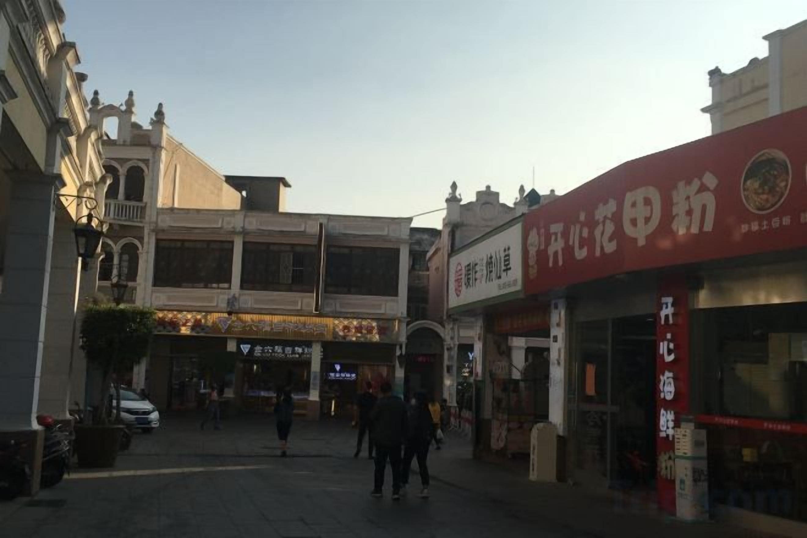 A street with buildings, a sign for a restaurant, and a few people walking.