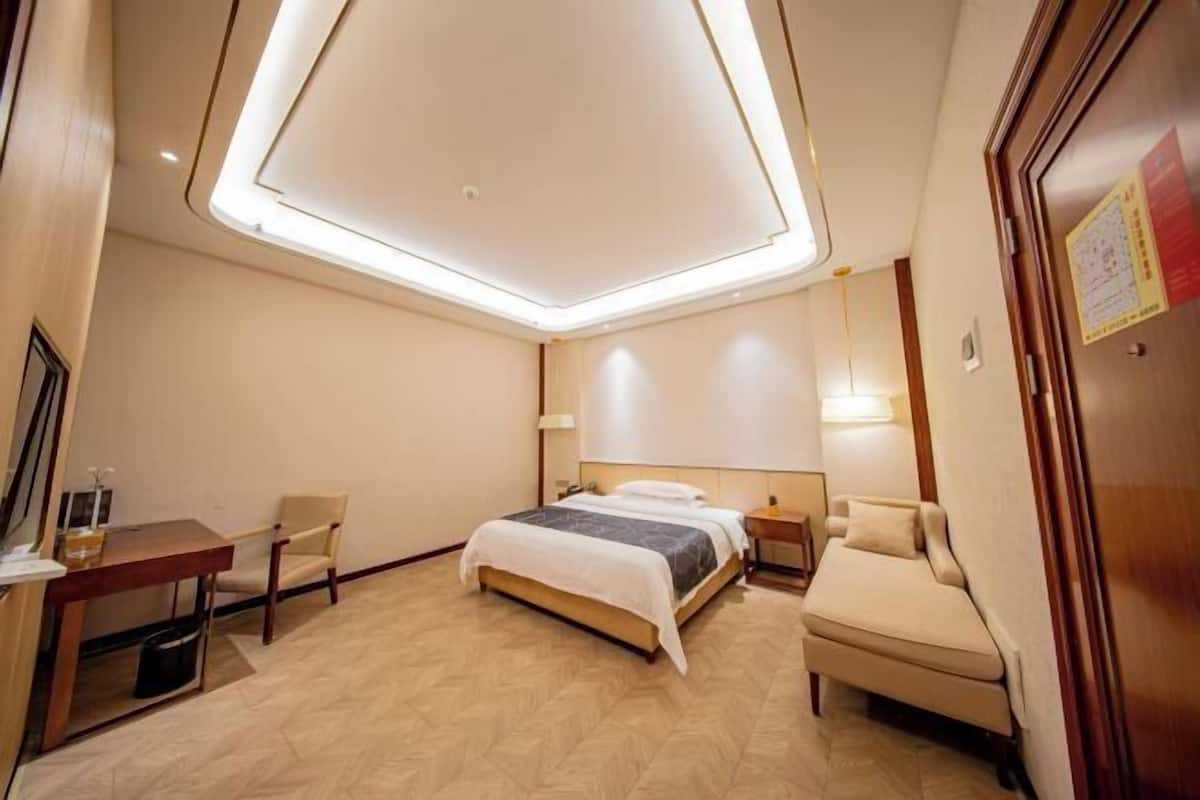 Een hotelkamer met een bed, een bureau, een stoel, een bijzettafeltje, een nachtkastje en een plafondlamp.