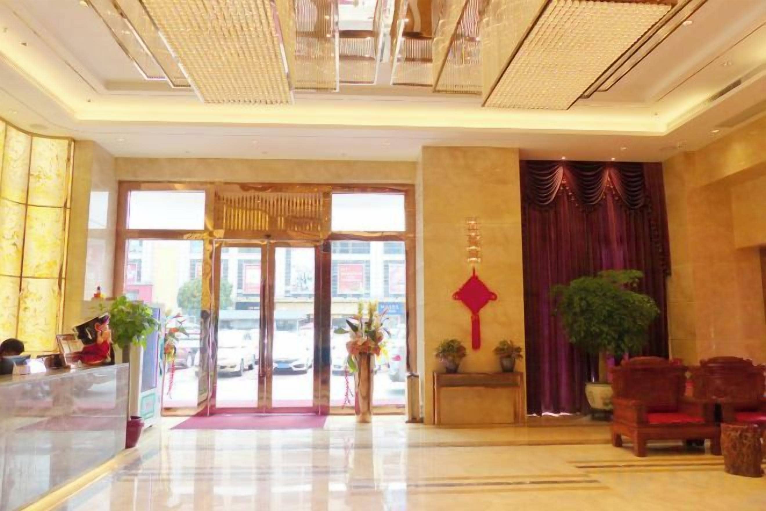 Un hall d’hôtel avec un comptoir d’accueil, un tapis rouge et une grande plante en pot.