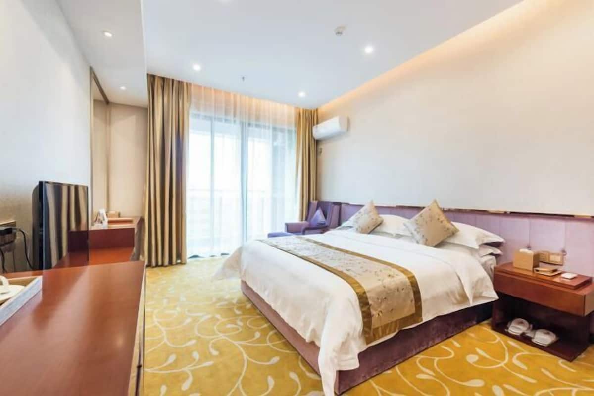 Een hotelkamer met een bed, een bureau, een stoel, een televisie en een raam met gordijnen.