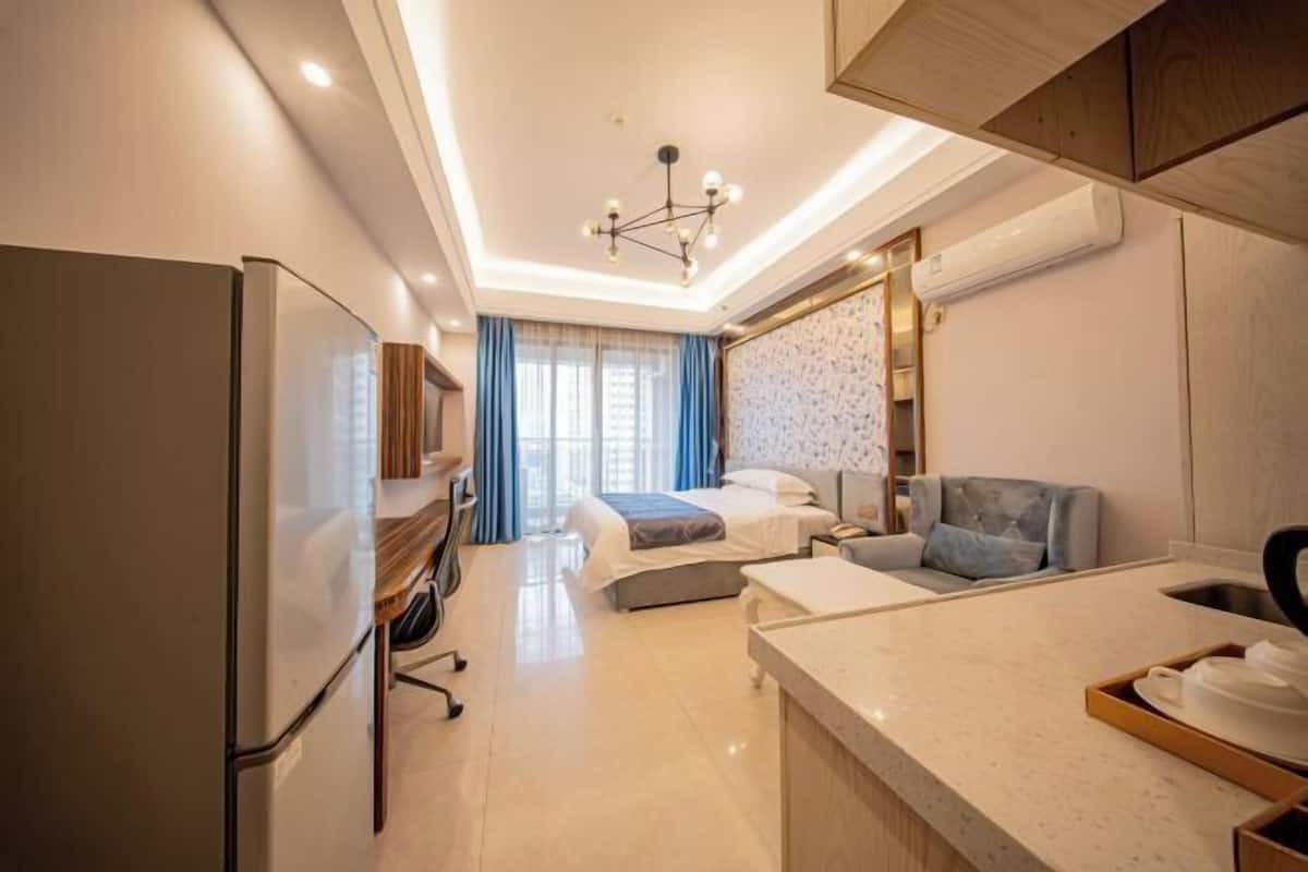 Hotelkamer met een bed, bureau, stoel, kitchenette en een groot raam met gordijnen.