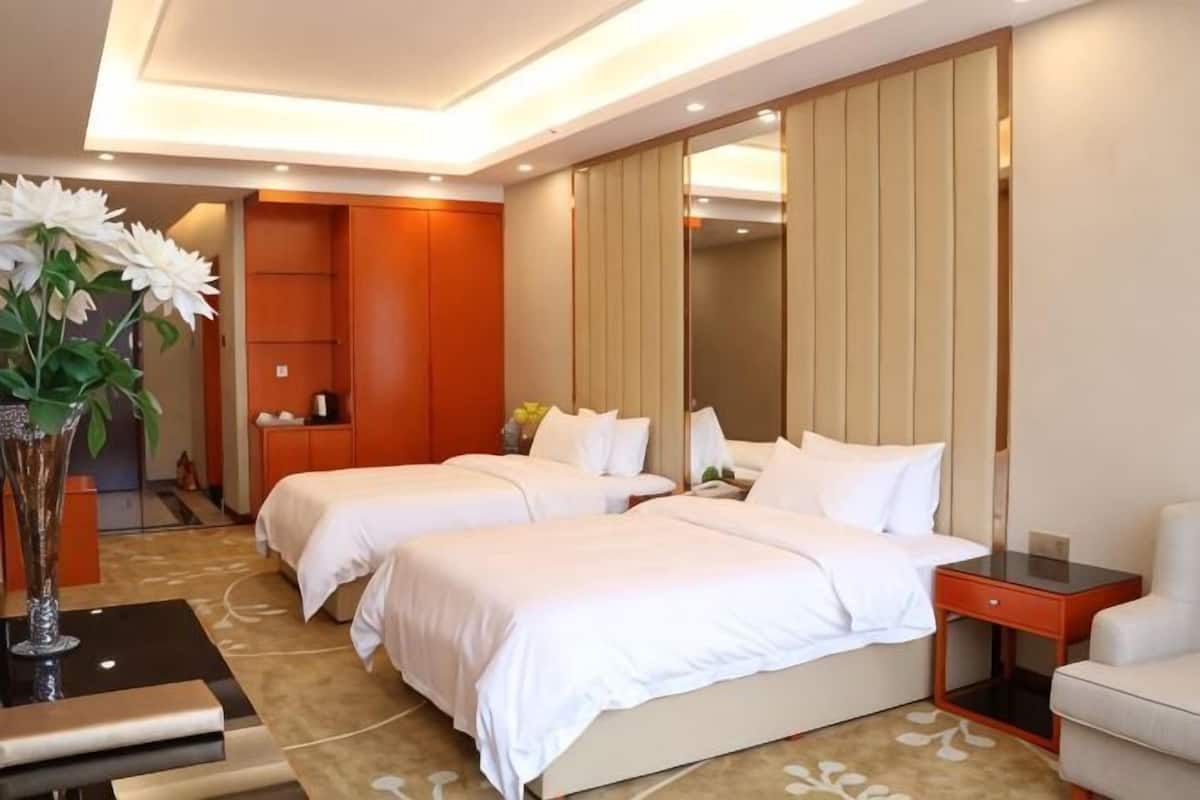 Een hotelkamer met twee bedden, een nachtkastje, een stoel, een bureau en een grote spiegel.
