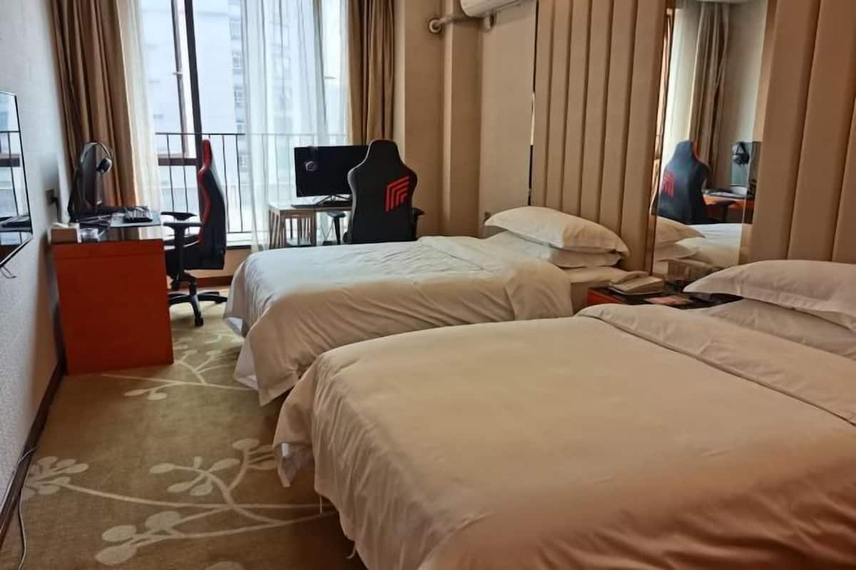 Een hotelkamer met twee bedden, een bureau met een computer, een stoel en een raam met gordijnen.