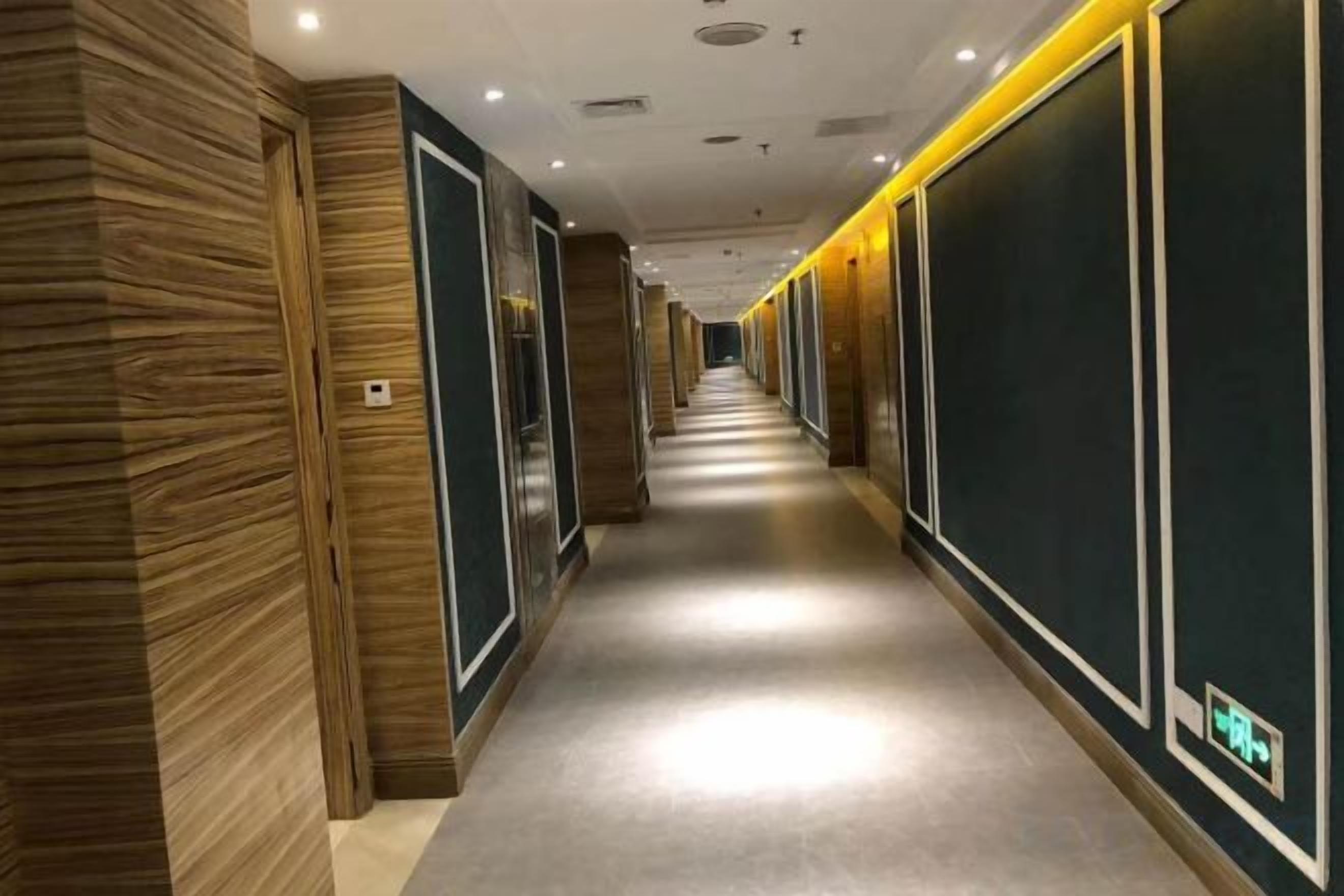 A hotel corridor with wooden paneling on the left, a central walkway, and dark paneling on the right.