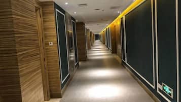 A hotel corridor with wooden paneling on the left, a central walkway, and dark paneling on the right.