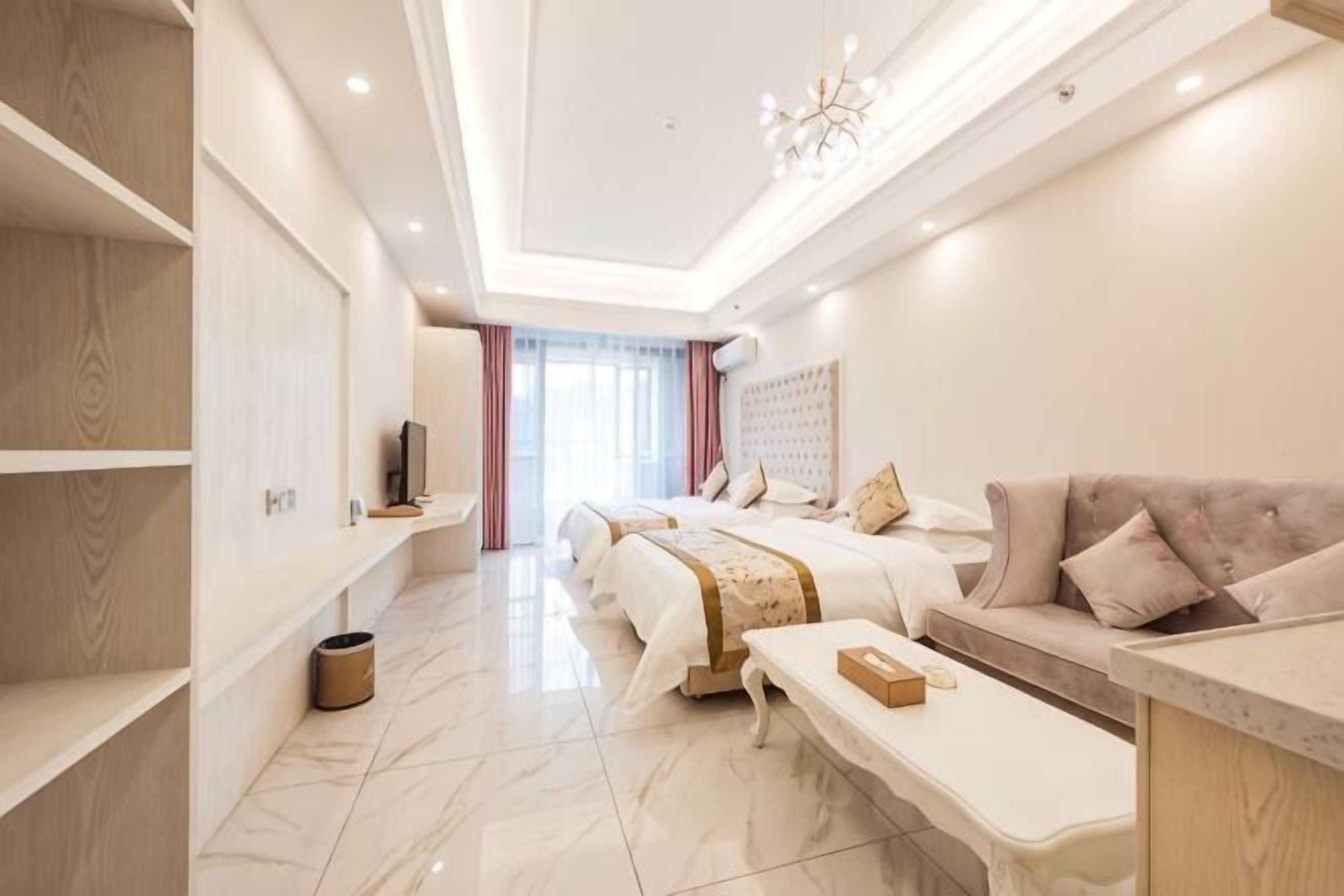 A hotel room with a bed, a sofa, a TV, a desk, and a window.