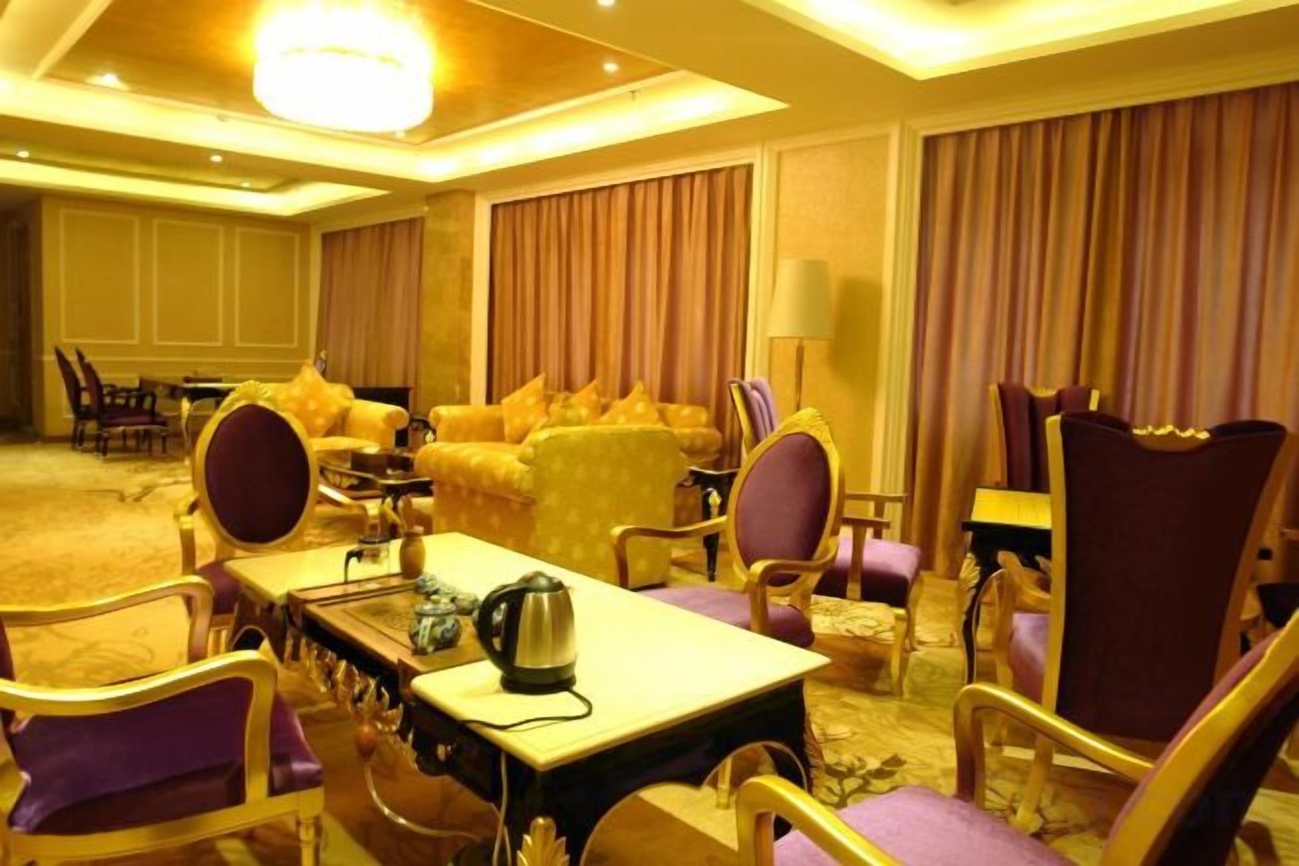 Habitación de hotel con una cama grande, una zona de estar con sofá y sillas, una mesa de comedor y una araña.
