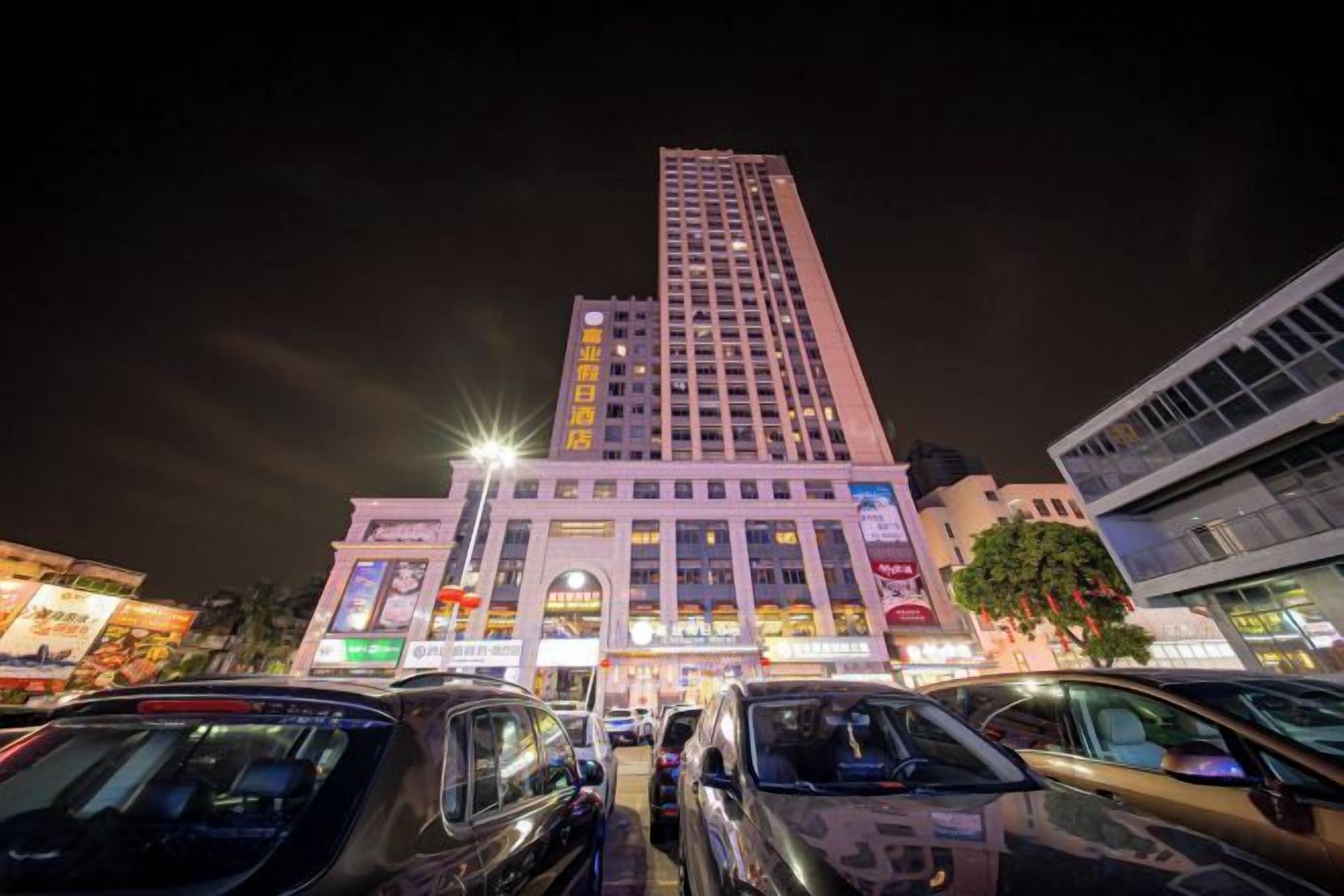 A multi-story building with illuminated signage, a parking lot with cars, and a clear night sky.