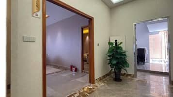 A hallway with a marble floor, a potted plant, and a door with a number sign.