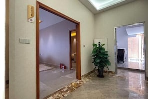 Un pasillo con piso de mármol, una planta en maceta y una puerta con el número.