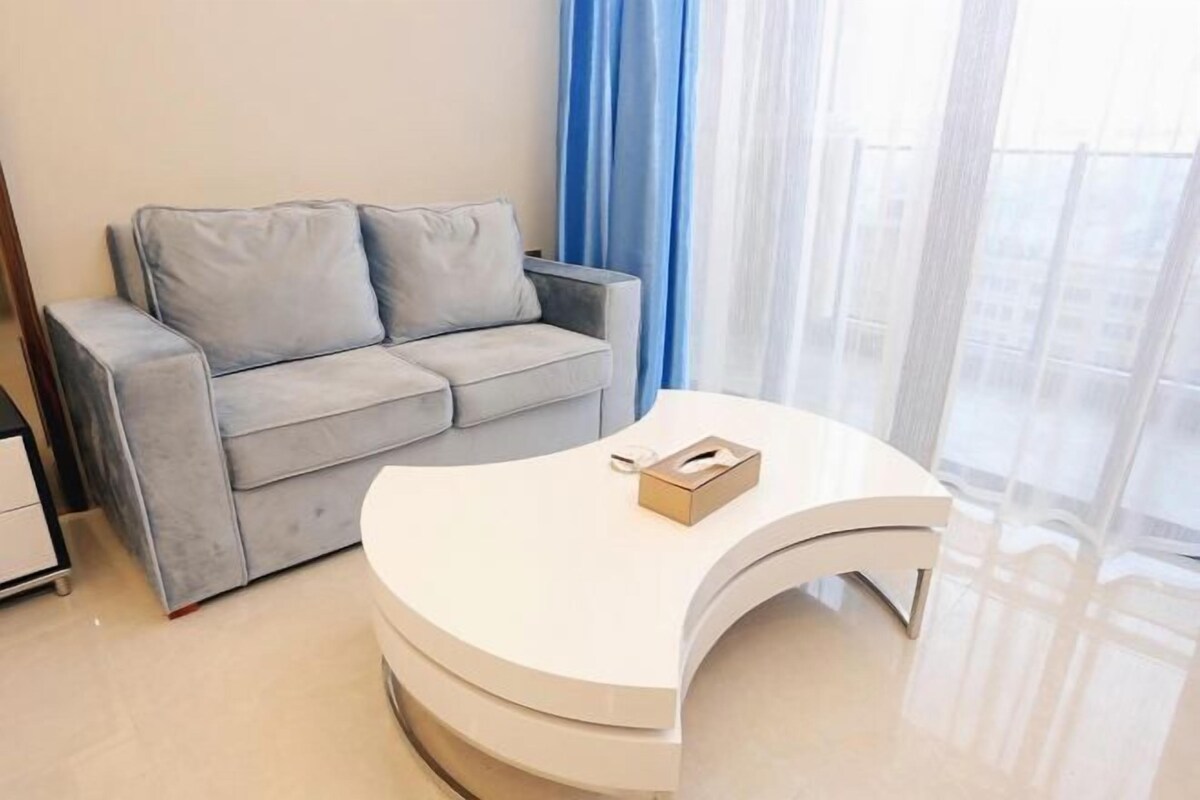 A modern living room with a grey sofa, a white curved coffee table, and a window with blue curtains.
