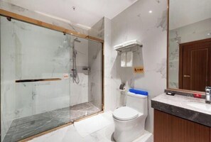 A bathroom with a glass-enclosed shower, a toilet, and a marble countertop.