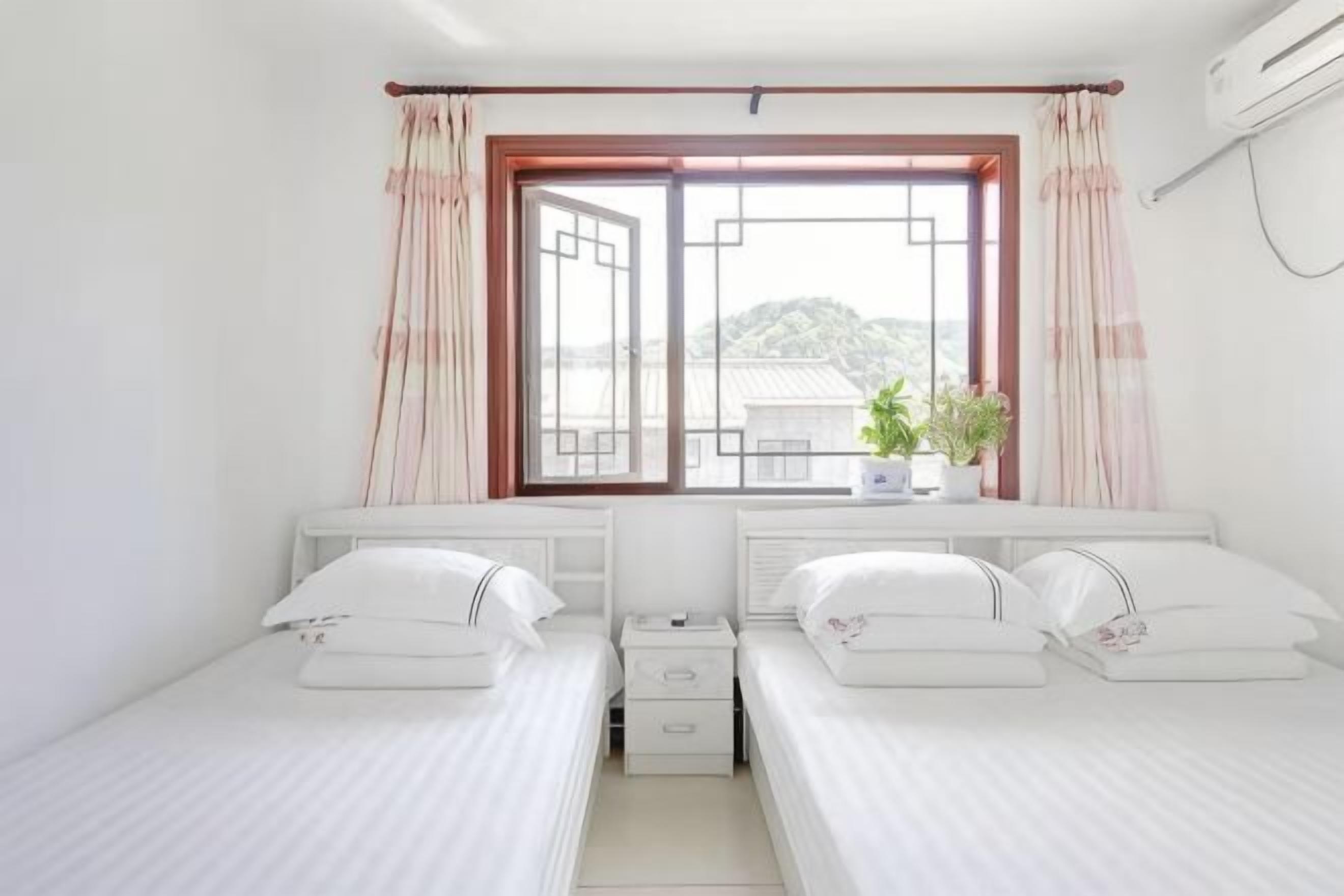 Quarto duplo com duas camas, janela com cortinas, mesa de cabeceira com planta e ar condicionado fixado na parede.