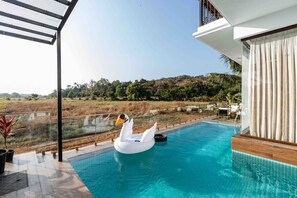 A swimming pool with a swan float, surrounded by a wooden deck and a white building with a balcony. - Luxury 4bhk Pool Villa - Sunset View (Candolim)
