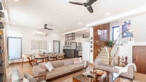 Ein großzügiger Wohnbereich mit Sofa, Couchtisch und Esstisch. Im Hintergrund befindet sich eine moderne Treppe und eine Küche.