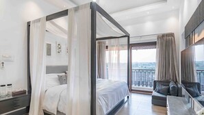 Ein modernes Schlafzimmer mit Himmelbett, einem Balkon mit Blick und einer Sitzecke mit Sofa und Tisch.