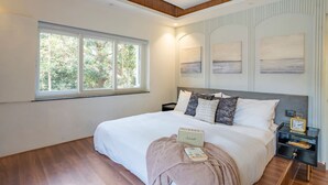 Een slaapkamer met een groot bed, een nachtkastje, een raam met uitzicht op bomen en decoratie aan de muur.