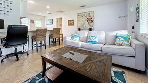 A modern living room with a white sofa, two armchairs, a coffee table, and a TV.