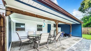 A covered patio with a table and chairs, a blue wall, and a wooden deck.