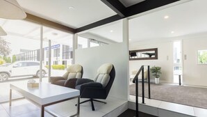 A modern hotel lobby with a reception desk, two chairs, a large window, and a staircase. - Grand Riccarton Hotel (Christchurch)