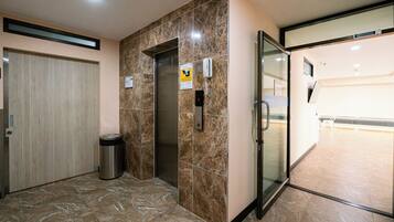 Un ascensor con pared de mármol, un cesto de basura y una puerta de vidrio que da a un pasillo.
