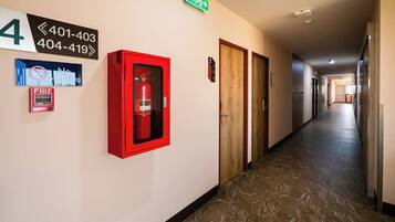 A hotel hallway with a fire extinguisher, emergency exit sign, and a no-smoking sign.