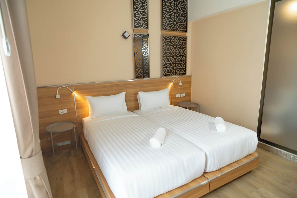 Una cama doble con sábanas blancas y dos almohadas, una mesita de noche y una lámpara de pared.