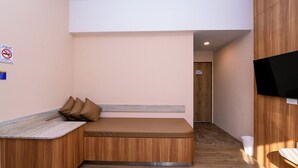 A room with a bench, a television mounted on the wall, and a door in the background. - One Budget Hotel Nan Pha Sing (Nan)