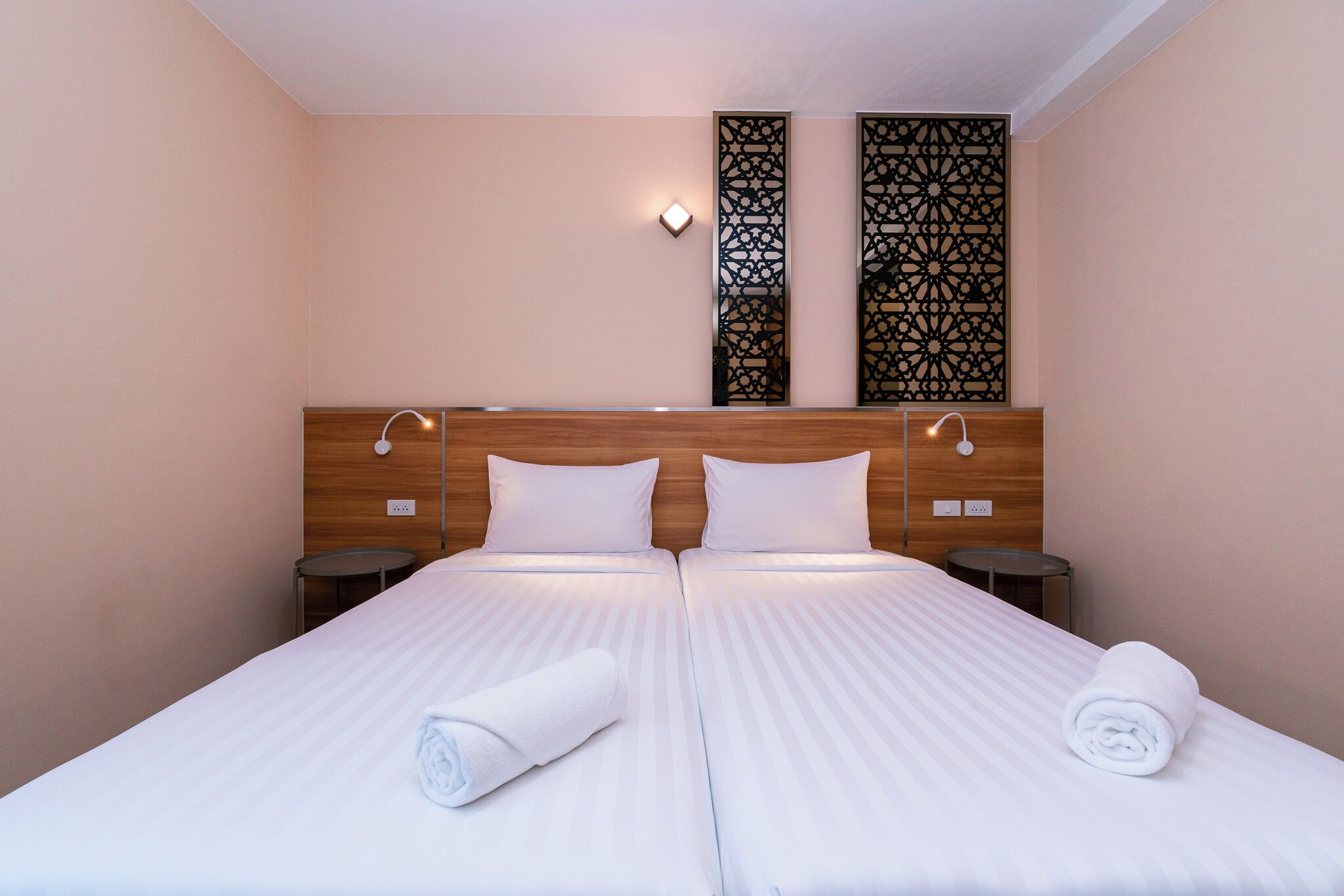 Una cama doble con ropa de cama blanca, dos mesitas de noche y paneles decorativos en la pared.