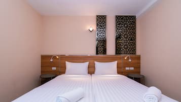 Una cama doble con ropa de cama blanca, dos mesitas de noche y paneles decorativos en la pared.
