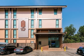 A building with a prominent 'one budget' sign, a covered entrance, and a parking area with cars and motorcycles. - One Budget Hotel Nan Pha Sing (Nan)
