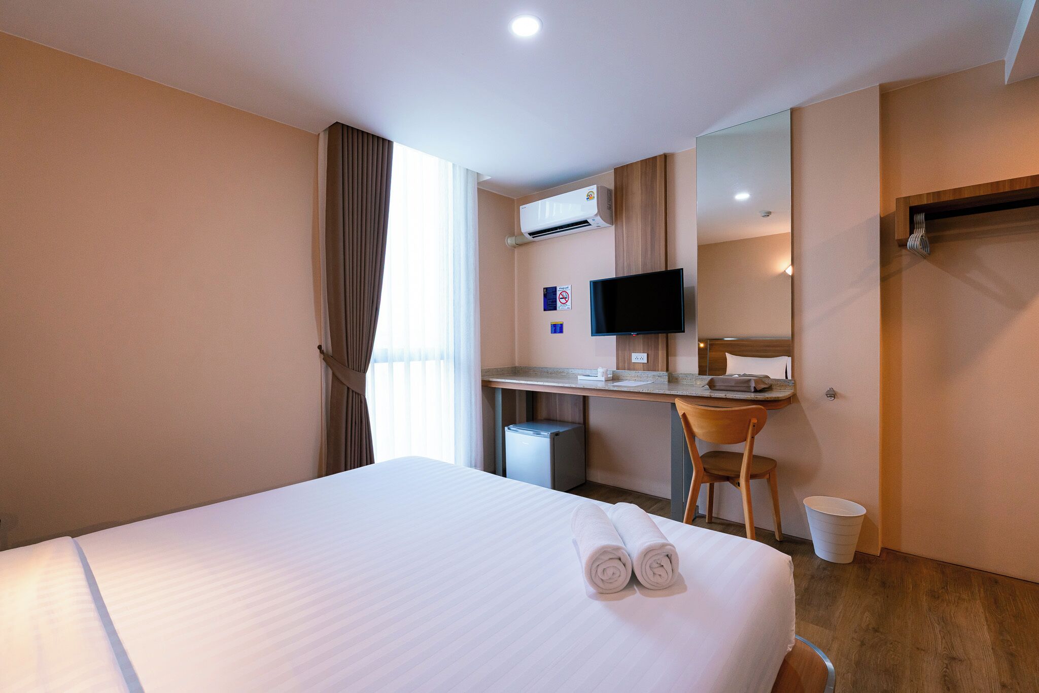A hotel room with a bed, a desk, a chair, a television, and a small trash bin.