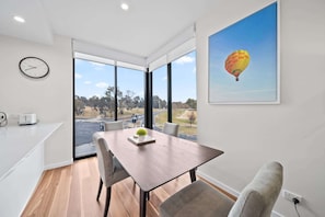 A modern dining area with a wooden table, grey upholstered chairs, a clock on the wall, and a hot air balloon painting.